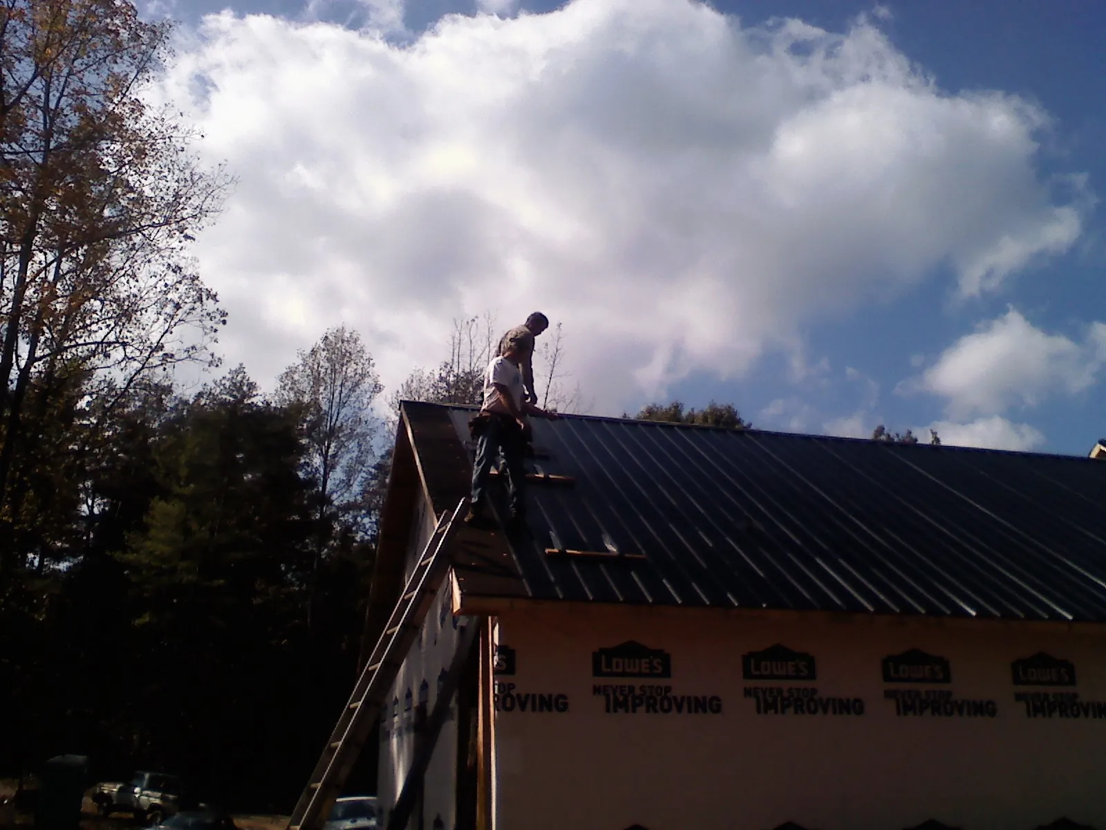 Roofer fastening dark metal panels high against a cloudy sky, from a Roof Inspection job in Scottsville
